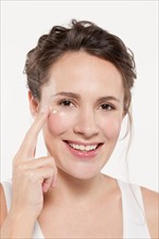 Portrait of woman applying face cream, studio shot. Photo : Jan Scherders