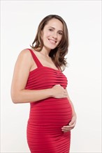 Portrait of pregnant woman in red dress, studio shot. Photo : Jan Scherders
