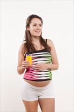 Portrait of pregnant woman holding glass of orange juice, studio shot. Photo : Jan Scherders