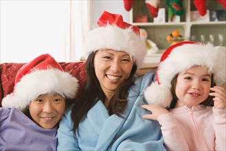 Portrait of mother with two daughters (10-11) wearing Santa hats. Photo : Rob Lewine
