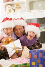 Portrait of father with two daughters (10-11) wearing Santa hats. Photo : Rob Lewine