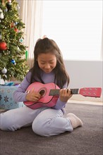 Girl (10-11) playing guitar, Christmas tree in background. Photo : Rob Lewine