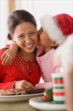 Girl (10-11) wearing Santa hat kissing mother. Photo : Rob Lewine