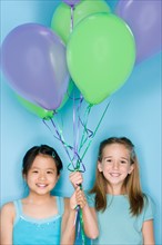 Studio portrait of two teenage (16-17) girls holding balloons. Photo : Rob Lewine