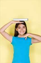 Studio portrait of teenage (16-17) girl balancing book on head. Photo : Rob Lewine