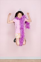 Studio shot portrait of jumping teenage girl in diadem and feather boa shawl, full length. Photo :