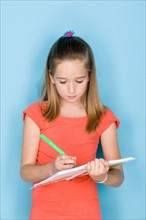 Studio shot portrait of teenage girl writing in notebook, waist up. Photo : Rob Lewine