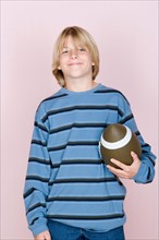 Studio shot portrait of teenage boy holding rugby ball, waist up. Photo : Rob Lewine