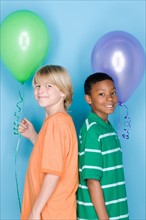 Studio shot portrait of two teenagers with balloons, waist up. Photo : Rob Lewine