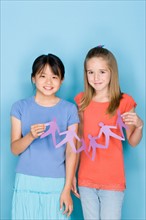 Studio shot portrait of two teenage girls holding paper chain, three quarter length. Photo : Rob
