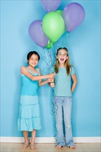 Studio shot portrait of two teenage girls holding balloons, full length. Photo : Rob Lewine