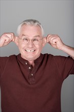 Studio shot portrait of senior man pulling his ears, head and shoulders. Photo : Rob Lewine