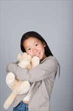 Studio portrait of teenage Chinese girl (16-17) hugging teddy bear. Photo : Rob Lewine
