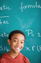 Happy young boy standing against blackboard after solving mathematical equation. Photo : Rob Lewine