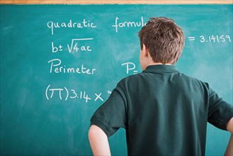 Boy standing in front of blackboard looking at mathematical formula. Photo : Rob Lewine