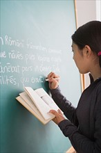 Schoolgirl writing on blackboard while holding book in her hand. Photo : Rob Lewine