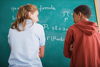Girl and boy standing in front of blackboard with mathematical formula. Photo : Rob Lewine