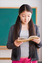 Schoolgirl reading book in front of blackboard. Photo : Rob Lewine
