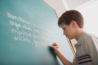 Boy writing Latin text on blackboard. Photo : Rob Lewine