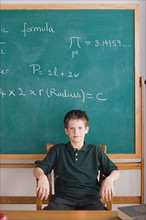 boy sitting in teachers chair, blackboard in background. Photo : Rob Lewine