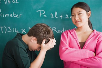 Happy girl and frustrated boy standing in front of blackboard with mathematical formula. Photo :