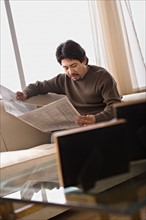 Mature man reading newspaper in living room. Photo : Rob Lewine