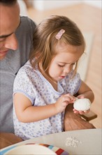 Girl sitting on father's lap peeling egg. Photo : Rob Lewine