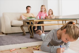 Girl drawing with family in background. Photo : Rob Lewine