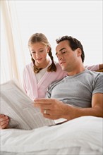 Father and daughter (12-13) reading newspaper in bedroom. Photo : Rob Lewine