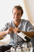 Smiling man opening bottle of wine. Photo : Rob Lewine