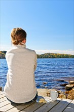 Canada, Ontario, Algonquin Park, Teenage girl sitting on pier and looking at lake. Photo :  Elena