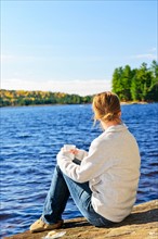 Canada, Ontario, Algonquin Park, Teenage girl sitting on rock and looking at lake. Photo :  Elena