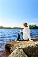 Canada, Ontario, Algonquin Park, Teenage girl sitting on rock and looking at lake. Photo :  Elena