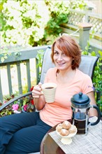 Smiling woman having coffee in garden. Photo : Elena Elisseeva