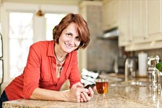 Canada. Ontario, Toronto, Woman in kitchen with glass of tea and cell phone. Photo : Elena