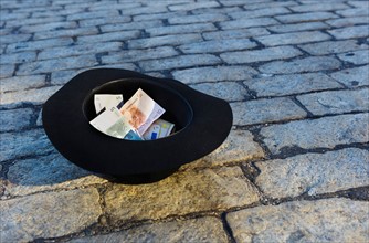 Money in hat on cobblestone street.