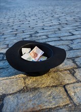 Money in hat on cobblestone street.