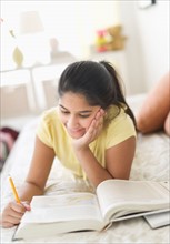 Girl (12-13) lying on bed and studying.