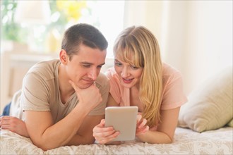 Couple lying on bed and using digital tablet.