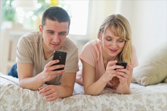 Couple lying on bed and using smart phones.