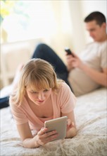 Couple lying on bed and using digital devices.