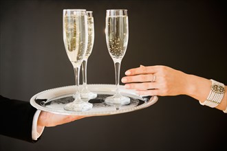 Close up of man's and woman's hands and tray with champagne flutes, studio shot. Photo : Jamie