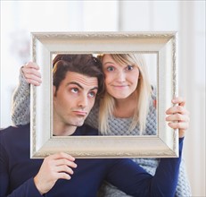 Couple holding picture frame and making faces. Photo : Daniel Grill