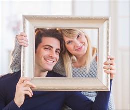 Portrait of smiling couple holding picture frame. Photo : Daniel Grill