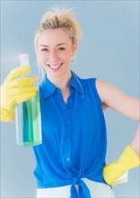 Portrait of young woman spraying cleaning detergent, studio shot. Photo : Daniel Grill