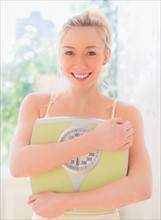 Portrait of smiling young woman holding weight scale. Photo : Daniel Grill