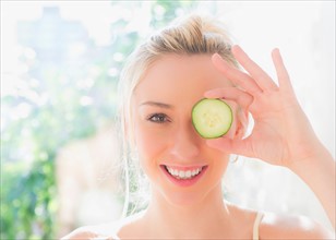 Portrait of smiling young woman covering eye with slice of cucumber. Photo : Daniel Grill
