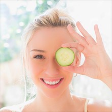 Portrait of smiling young woman covering eye with slice of cucumber. Photo : Daniel Grill