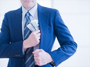 Businessman hiding banknotes in pocket. Photo : Daniel Grill