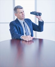 Portrait of businessman holding binoculars. Photo : Daniel Grill